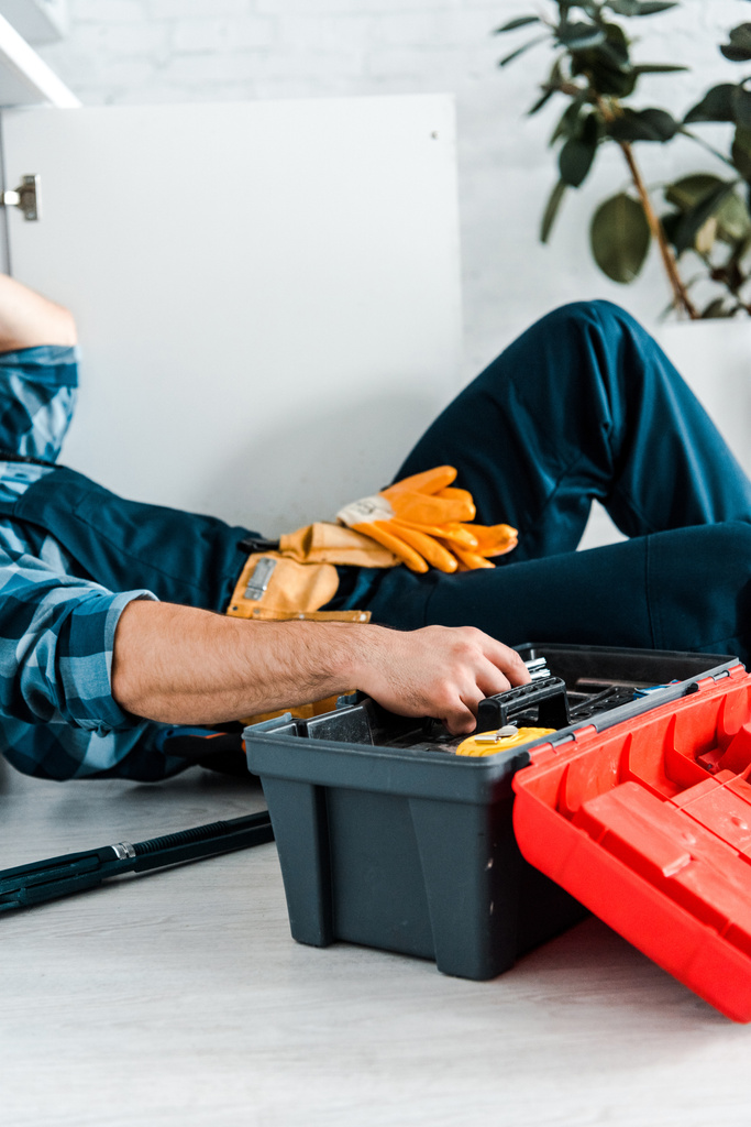 vista recortada del reparador que trabaja en la cocina cerca de la caja de herramientas mientras está acostado en el suelo
  - Foto, imagen