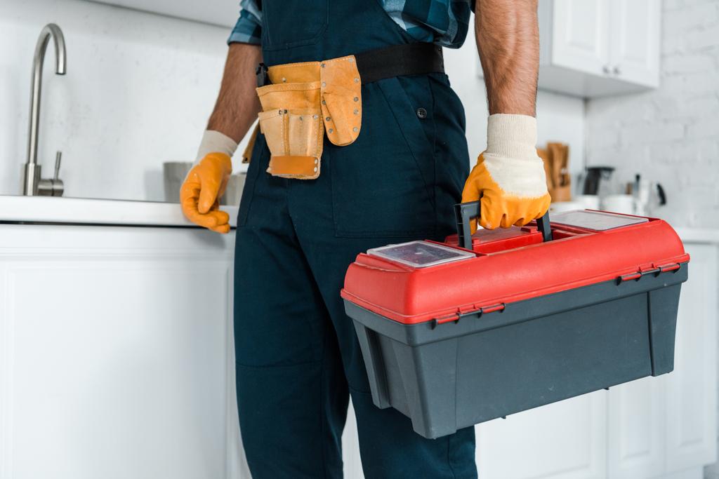 vista recortada del trabajador en pie uniforme y caja de herramientas de retención
  - Foto, imagen