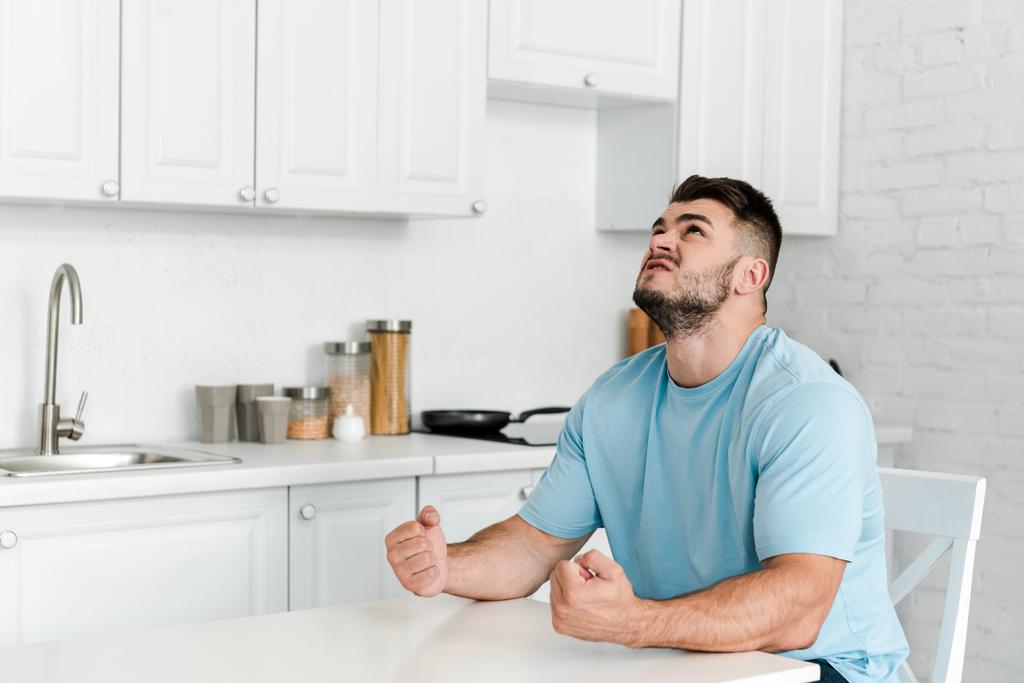 сердитый мужчина жестом, сидя рядом со столом на кухне
  - Фото, изображение