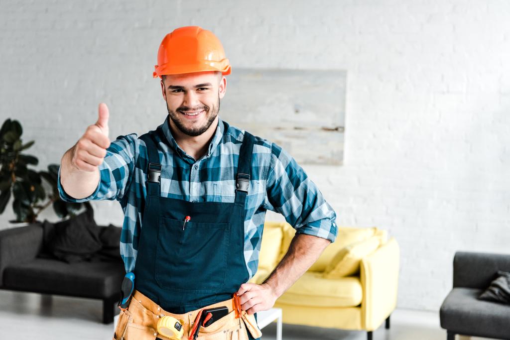 cheerful worker in safety helmet looking at camera while showing thumb up  - Photo, Image