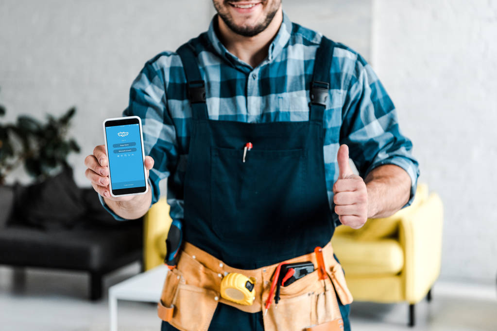 キエフ、ウクライナ - 2019年7月31日:画面上のSkypeアプリでスマートフォンを保持し、親指を表示する幸せな男のトリミングビュー  - 写真・画像