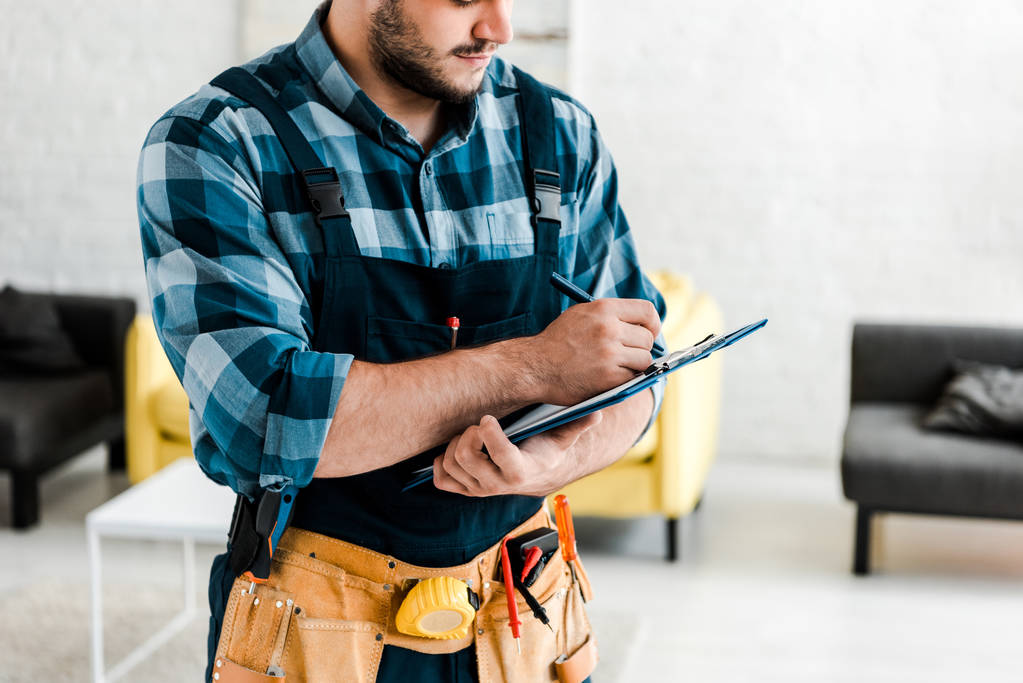 cropped view of bearded worker writing while holding clipboard  - Photo, Image