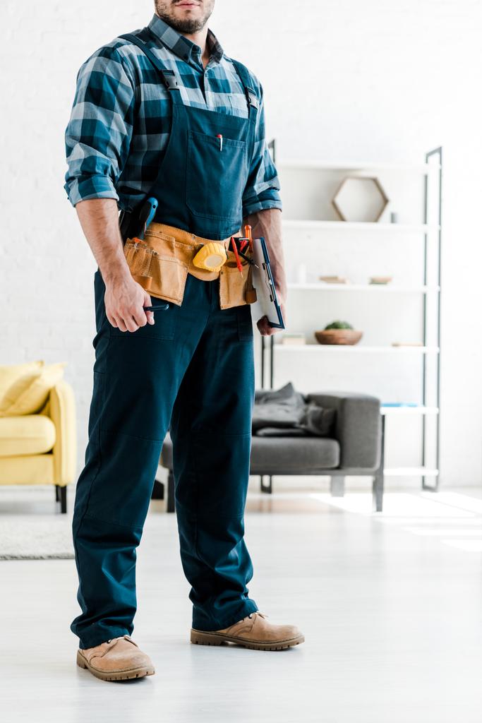 cropped view of bearded worker in safety helmet holding clipboard in living room  - Photo, Image