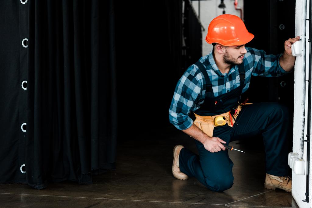όμορφος μουσάτος εργάτης σε κράνος ασφαλείας αγγίζοντας διακόπτη φωτισμού   - Φωτογραφία, εικόνα
