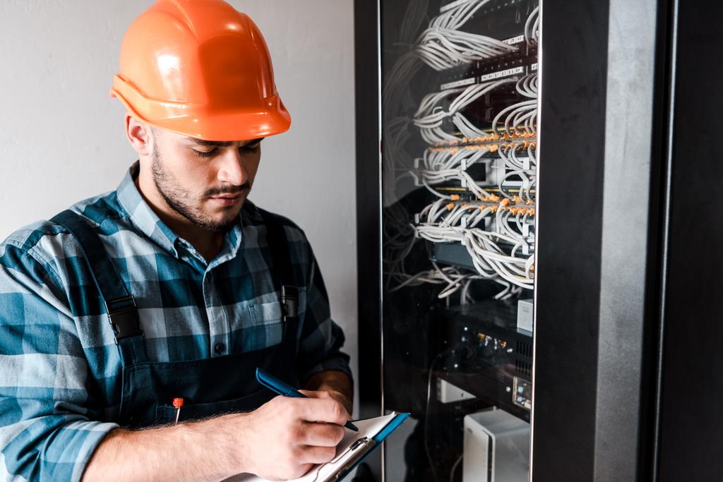 technician holding clipboard while writing near wires and cables  - Photo, Image