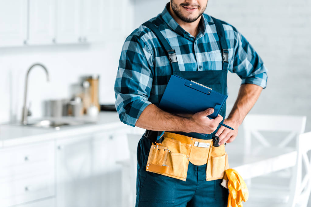 bijgesneden beeld van bebaarde workman staand met de hand op hip en holding Klembord  - Foto, afbeelding