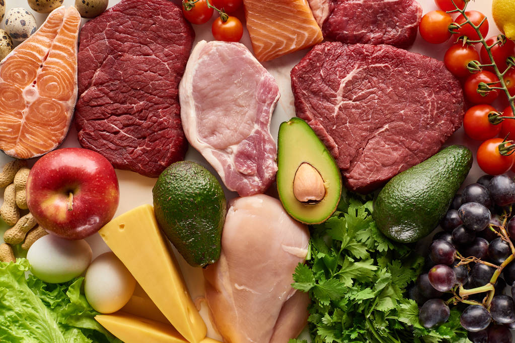 Вид сверху на разнообразное сырое мясо, птицу, рыбу, яйца, овощи, фрукты, орехи, зелень и сыр
  - Фото, изображение