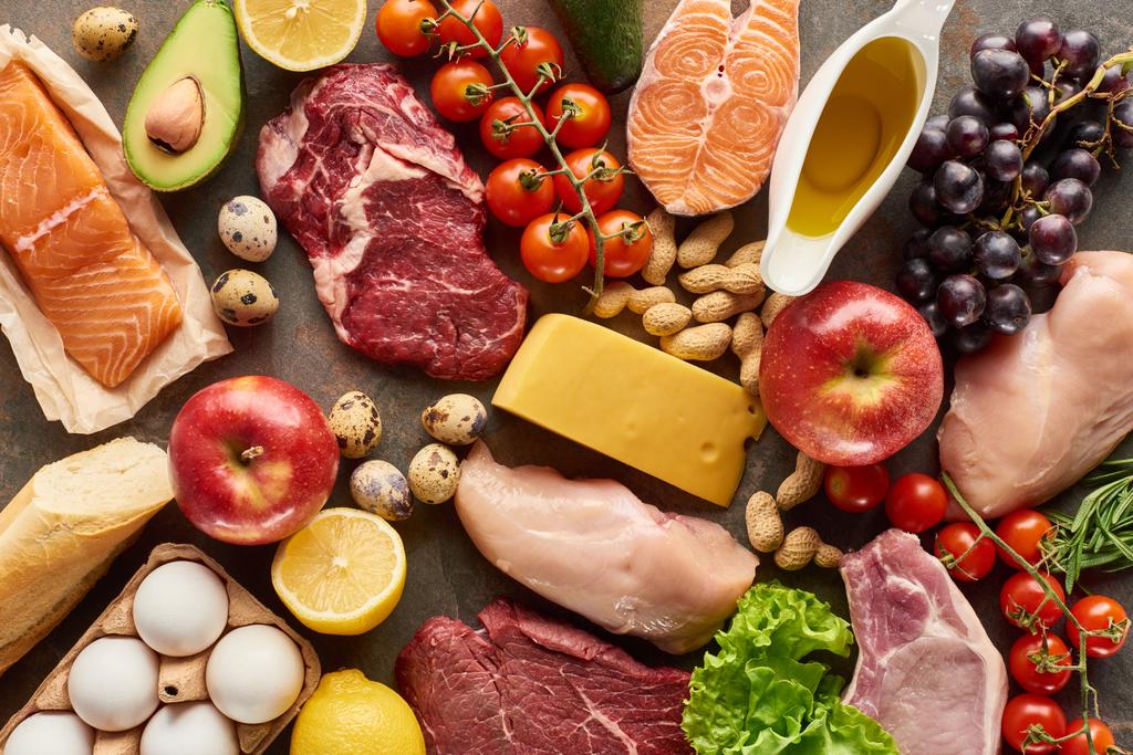 Top uitzicht van diverse vlees, gevogelte, vis, eieren, fruit, groenten, kaas, olijfolie en stokbrood - Foto, afbeelding