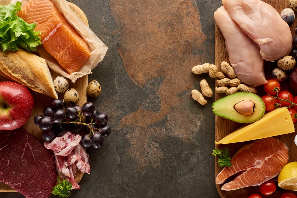 生肉、魚、家禽、チーズ、果物、野菜、ピーナッツネオンダークブラウン大理石表面と木製のまな板のトップビュー - 写真・画像