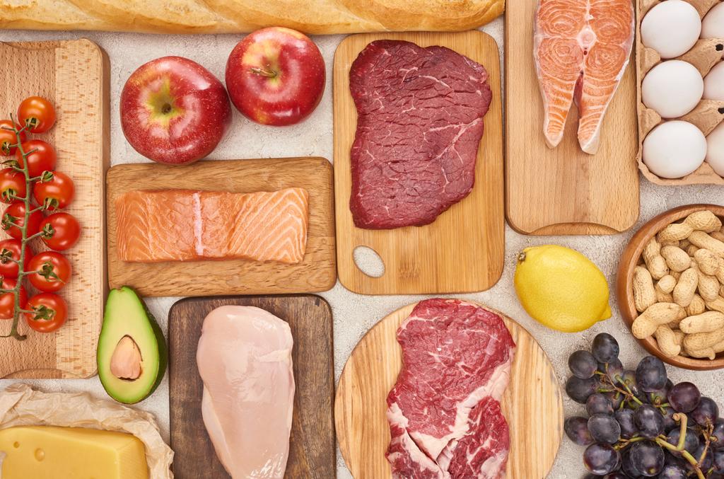 Top uitzicht van diverse vlees, gevogelte, vis, eieren, fruit, groenten, kaas en stokbrood op houten snijplanken - Foto, afbeelding