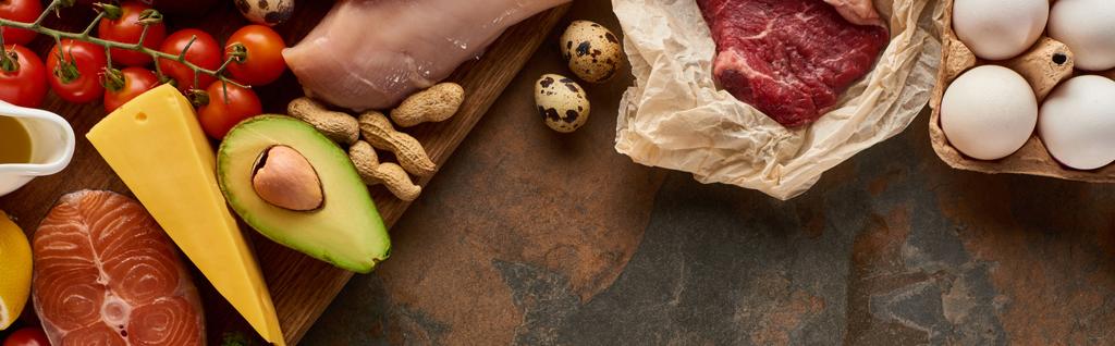 Foto panorámica de tabla de cortar de madera con pescado crudo y aves de corral cerca de verduras, queso, carne, huevos y cacahuetes en la superficie de mármol
 - Foto, Imagen
