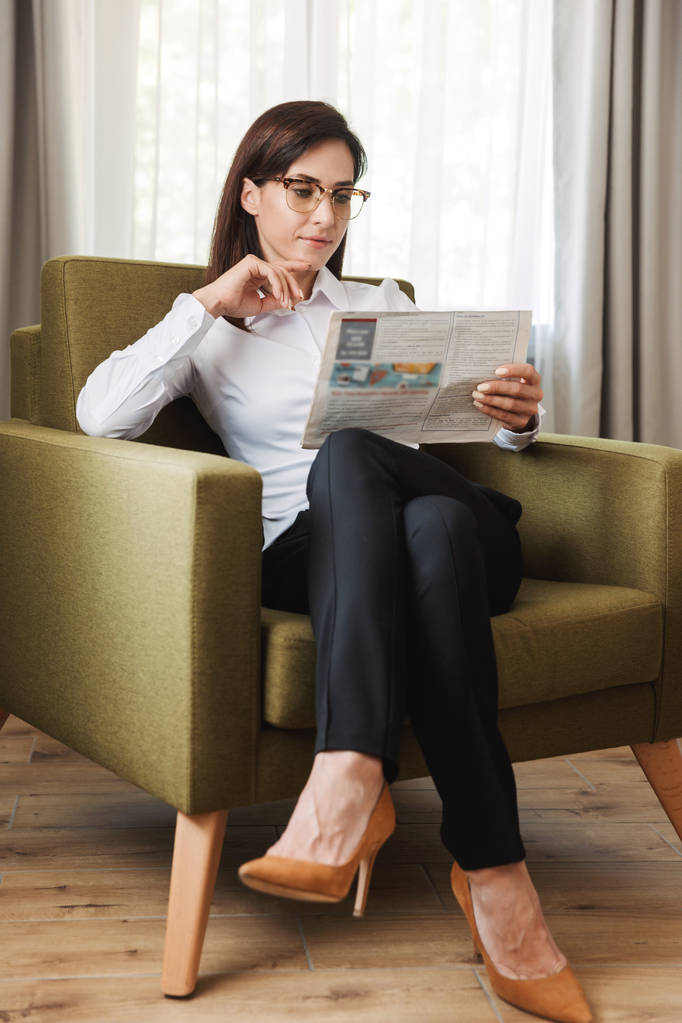 Koncentrovaná krásná mladá obchodní žena ve formálním nošení oblečení doma pro čtení novin. - Fotografie, Obrázek