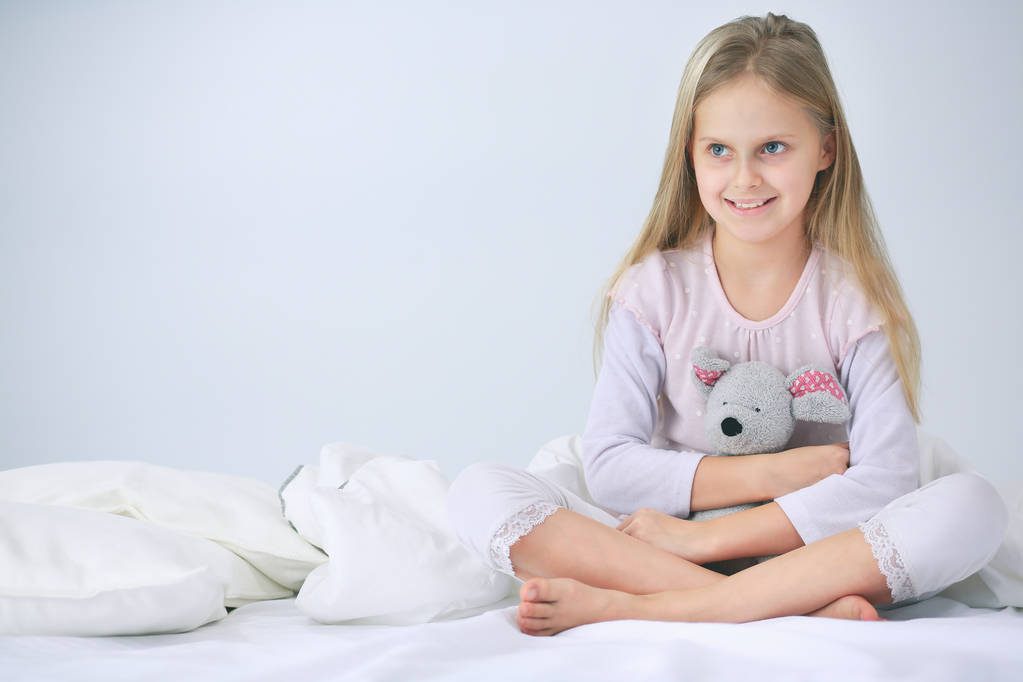 La petite fille dans la chambre est assise sur le lit. Petite fille porte un pyjama et assise au lit
 . - Photo, image