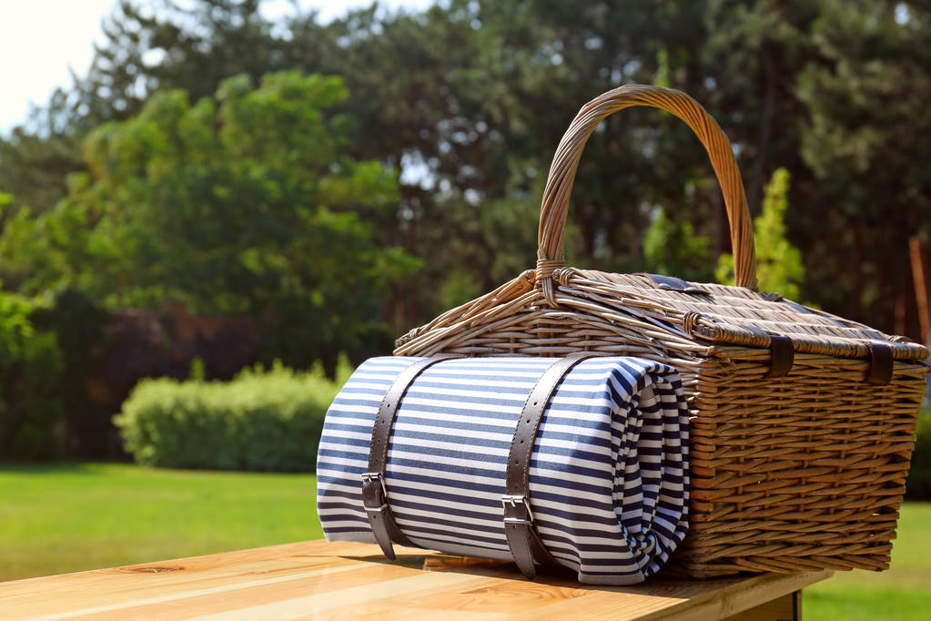 Panier pique-nique avec couverture sur table en bois dans un parc verdoyant
 - Photo, image