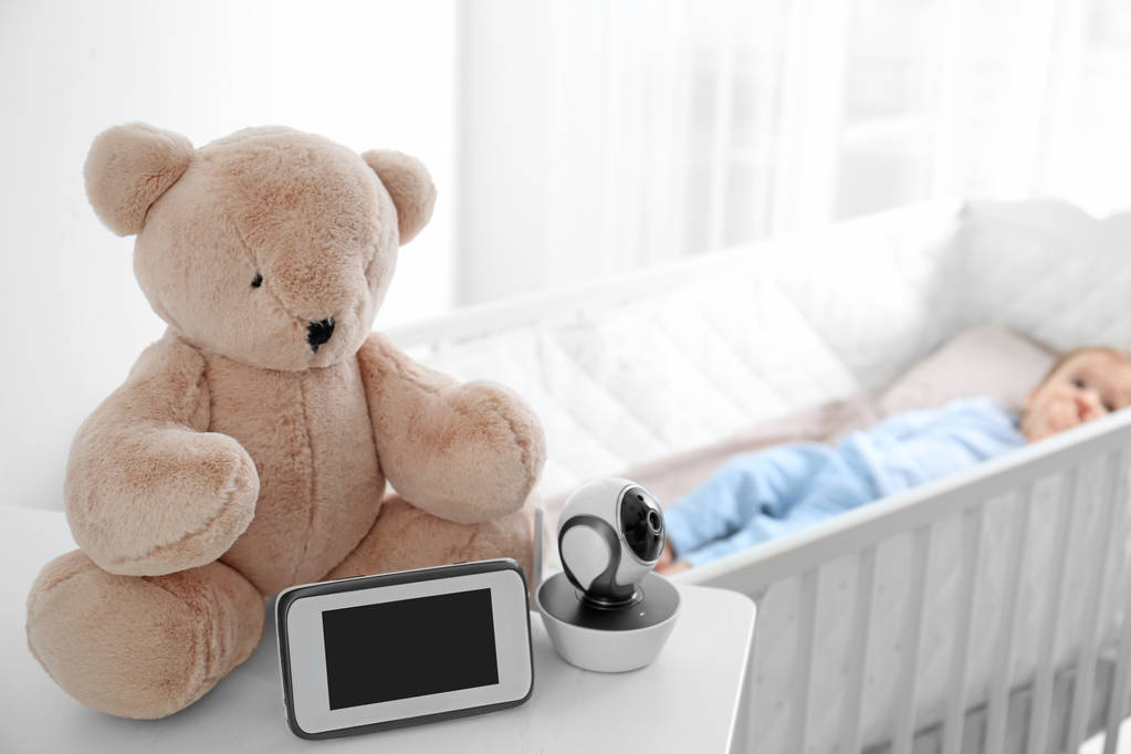 Baby Monitor, aparat fotograficzny i zabawka na stole w pobliżu łóżeczka z dzieckiem w pokoju. Niania wideo - Zdjęcie, obraz
