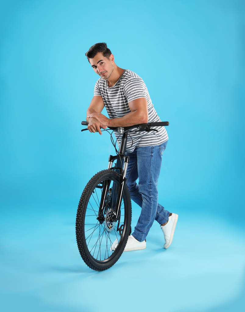Pohledný mladý muž s moderním bicykl na světle modrém pozadí - Fotografie, Obrázek