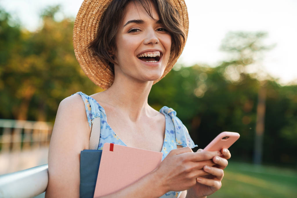 Όμορφη ευτυχισμένη νεαρή όμορφη γυναίκα σε πράσινο πάρκο σε εξωτερικούς χώρους χρησιμοποιώντας το κινητό τηλέφωνο. - Φωτογραφία, εικόνα