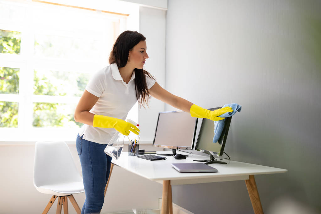 Jonge vrouw schoonmaken computer met blauwe servet in Office - Foto, afbeelding
