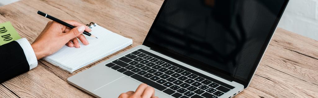 tiro panorâmico de mulher segurando caneta ao usar laptop com tela em branco
  - Foto, Imagem