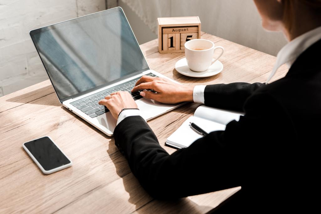 selectieve focus van vrouw typen op laptop in de buurt van houten kubussen met kalender en smartphone met leeg scherm  - Foto, afbeelding