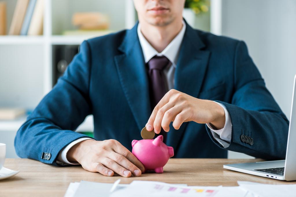 cropped view of businessman putting metallic coin into pink piggy bank  - Photo, Image