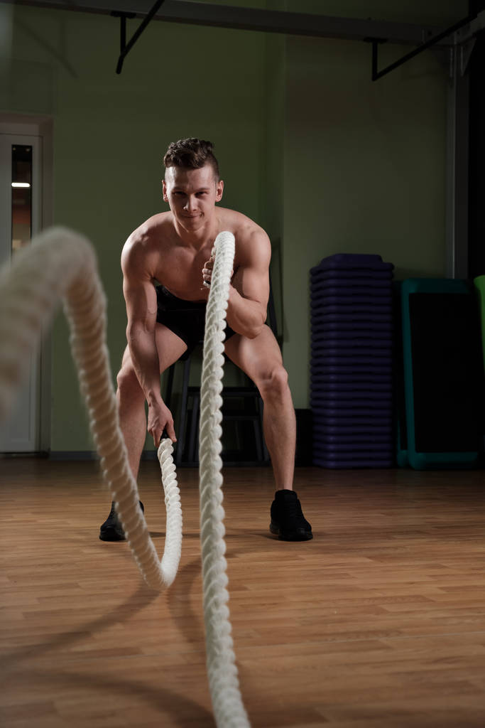 Homme adulte athlétique avec corde de combat faisant de l'exercice dans un gymnase d'entraînement fonctionnel - Photo, image