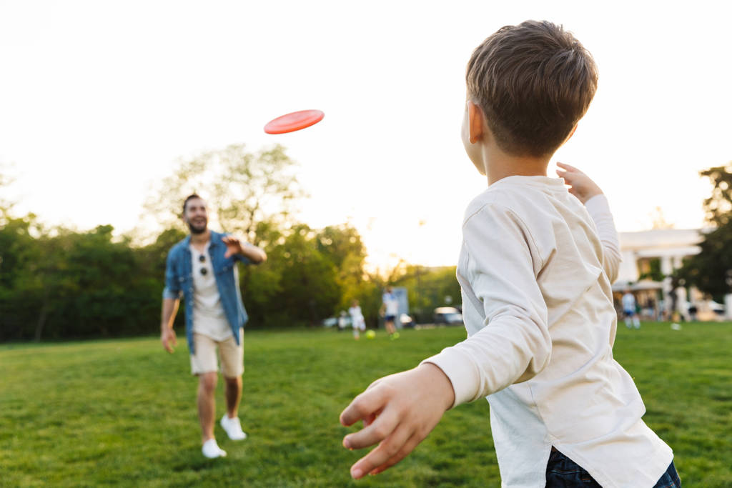 Jonge man met plezier met zijn kleine broer of zoon outoors in Park mooie groene gras spelen spel. - Foto, afbeelding