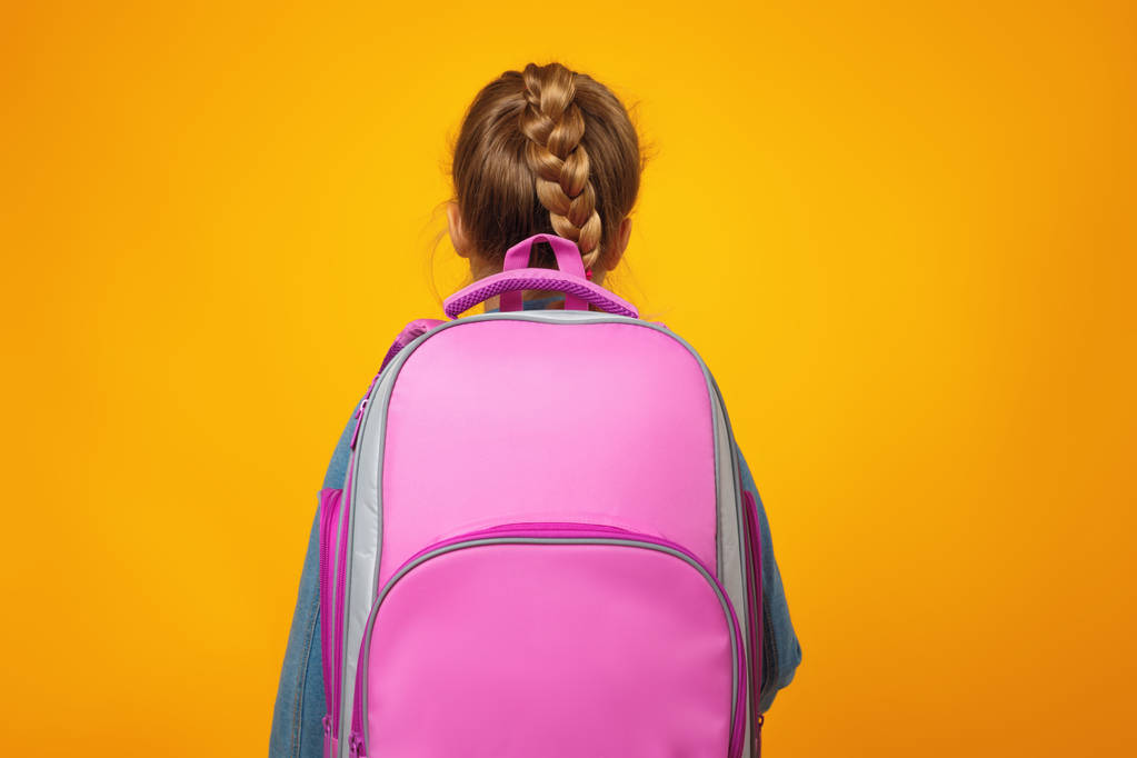 Küçük kız öğrenci sarı bir arka plan üzerinde sırtı ile duruyor. Çocuğun elinde bir çanta var. Okul ve eğitim kavramı. - Fotoğraf, Görsel