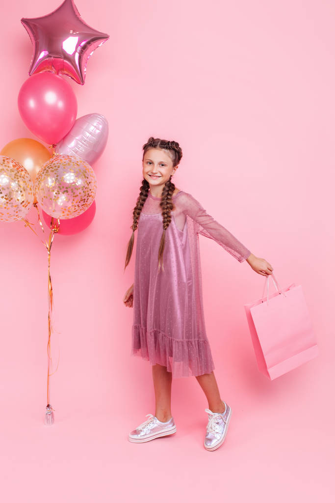 Boldog lány léggömbök és bevásárló táskák pózol egy rózsaszín vissza - Fotó, kép