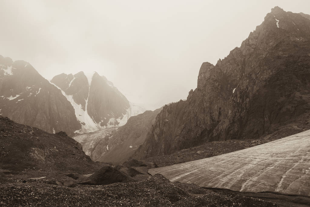 Un grand nombre de pierres sur le dessus. Les sommets des montagnes dans les nuages brumeux. Belle vue sur les hautes montagnes enneigées et un glacier lors d'un voyage touristique à travers la nature du territoire de l'Altaï. Photo sépia tonique
. - Photo, image