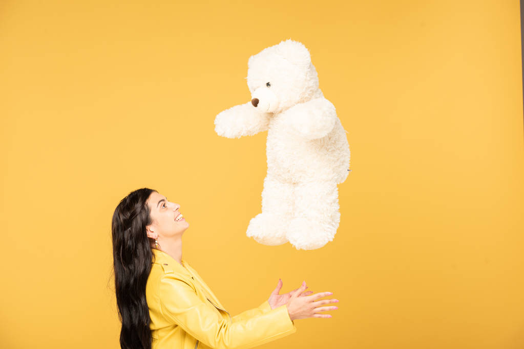приваблива весела жінка кидає плюшевого ведмедя, ізольована на жовтому
 - Фото, зображення
