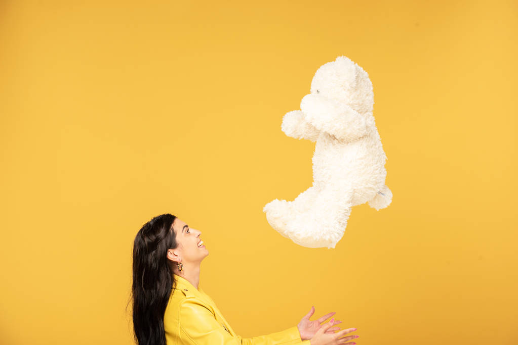 beautiful young woman throwing up teddy bear, Isolated On yellow - Photo, Image