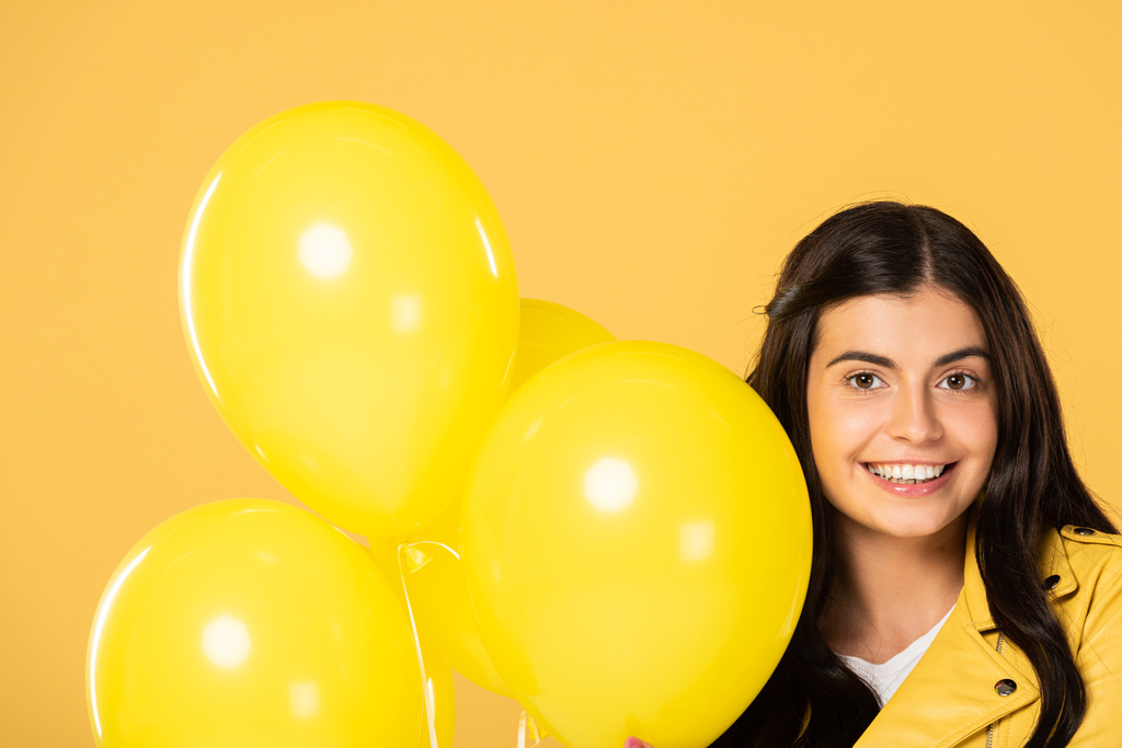 atractiva chica sonriente sosteniendo globos amarillos, aislado en amarillo
 - Foto, Imagen