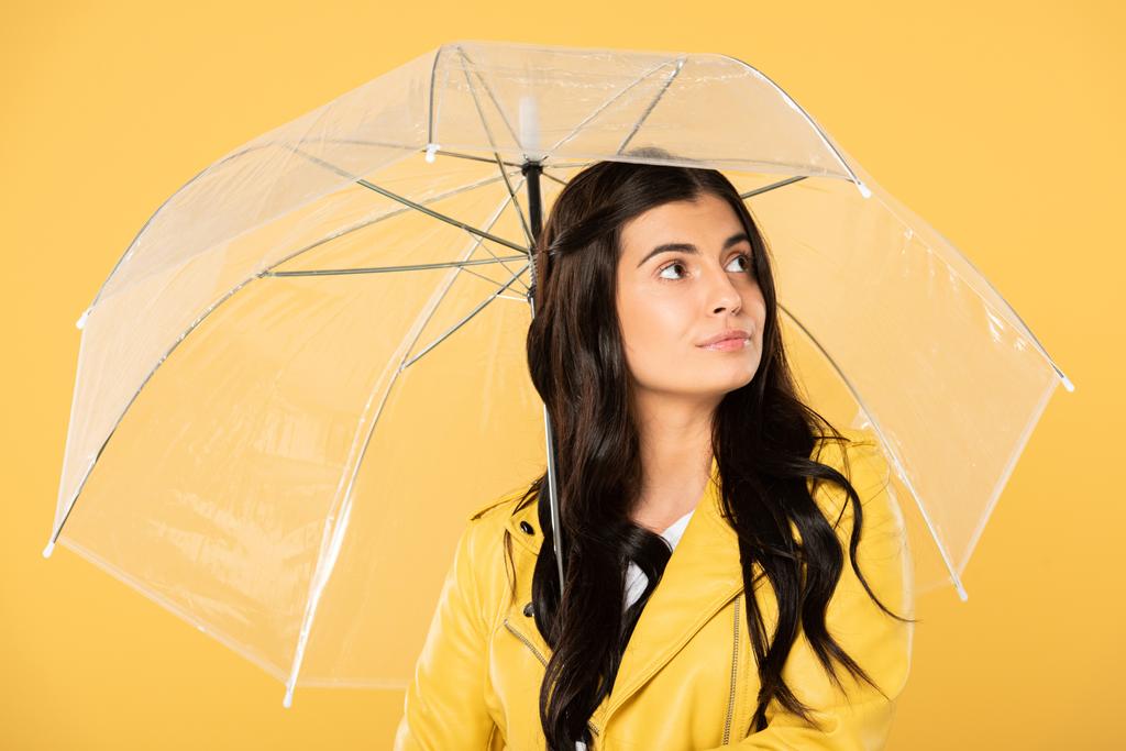 piękny zamyślony kobieta stwarzające z przezroczystym parasolem, izolowane na żółtym - Zdjęcie, obraz