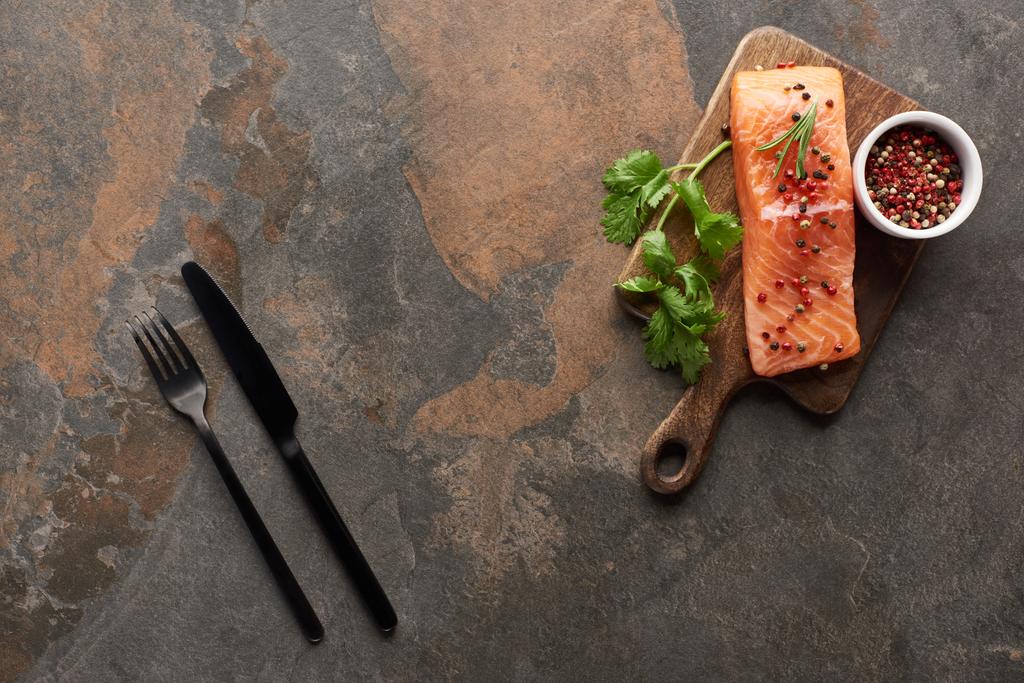 vista superior de salmão fresco com pimenta, salsa em tábua de corte de madeira perto de talheres
 - Foto, Imagem