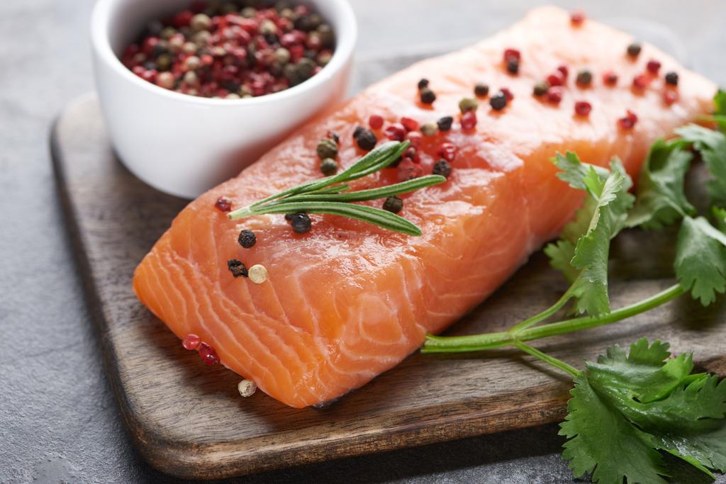 raw salmon with peppercorns, parsley and rosemary on wooden cutting board - Photo, Image