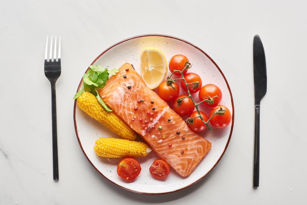 top view of raw salmon steak served with corn and tomatoes on plate near cutlery on marble table - Photo, Image