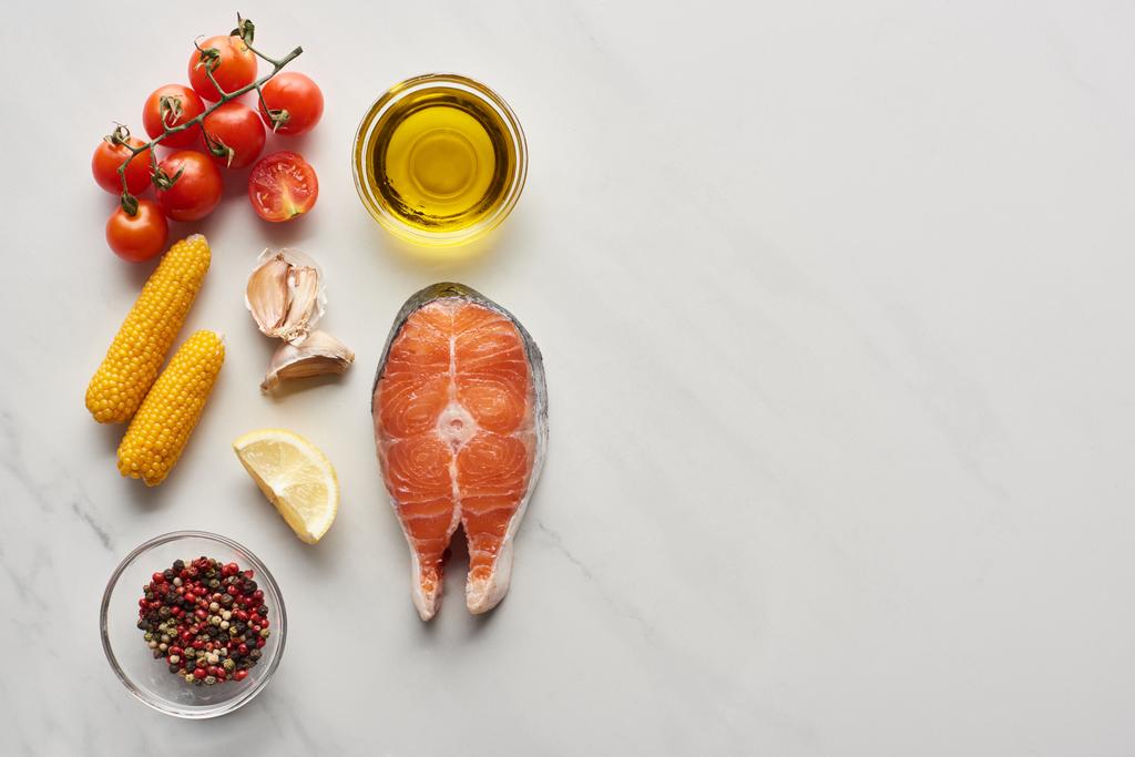 vista superior de bife de salmão não cozido perto de limão, milho, tomate, alho, óleo e pimenta em tigelas na mesa de mármore
 - Foto, Imagem