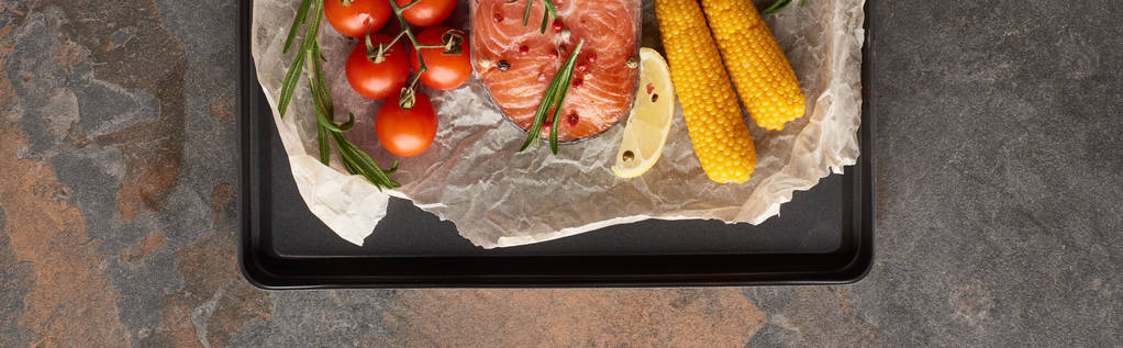 plano panorámico de filete de salmón sin cocer con tomates, maíz, romero, limón y pimienta sobre papel de panadería en bandeja de horno
 - Foto, imagen