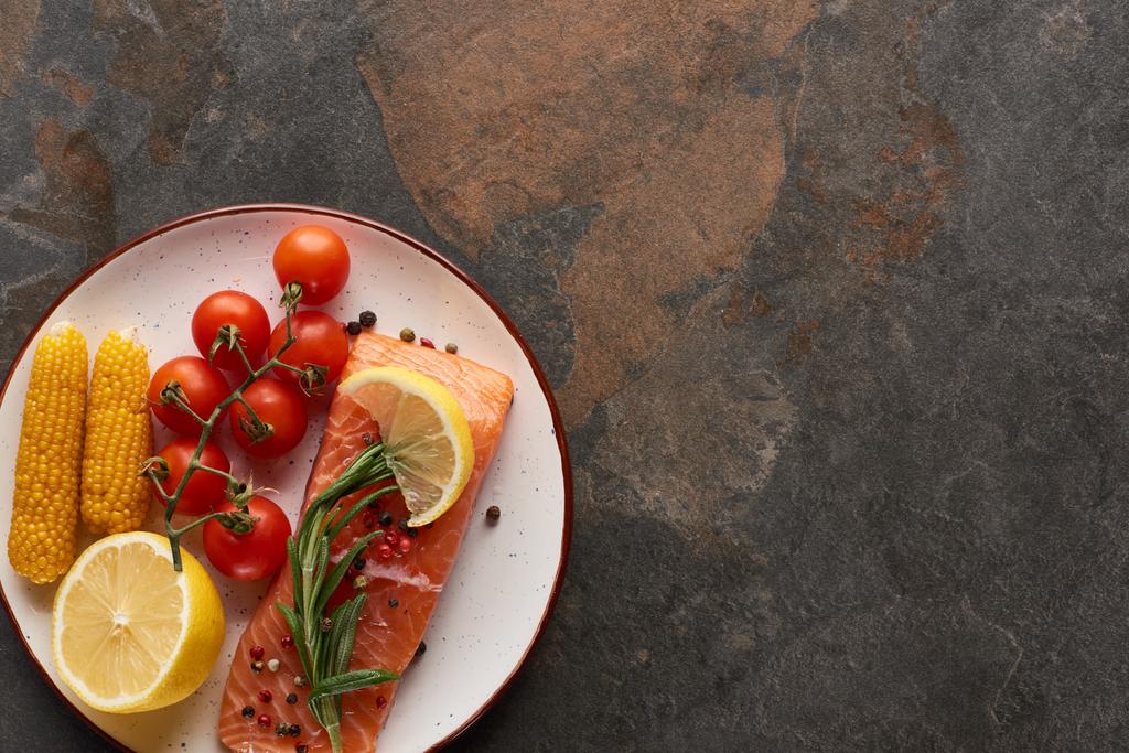 vista superior de bife de salmão não cozido com tomate, milho, limão, alecrim e pimenta no prato
 - Foto, Imagem