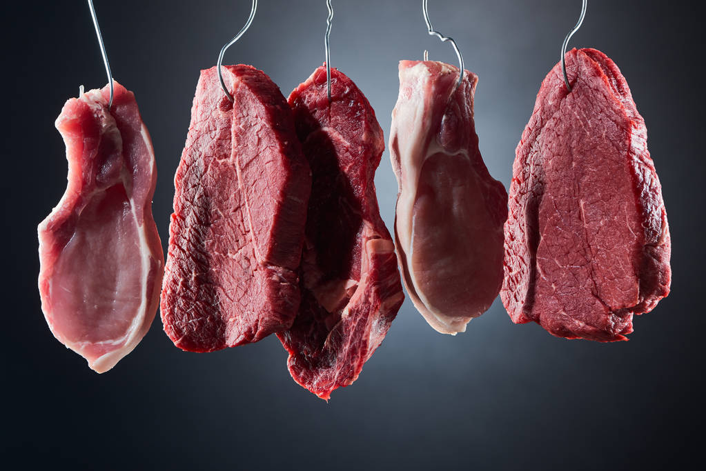 různé steaky z syrového masa na kovových háčků na černém pozadí - Fotografie, Obrázek