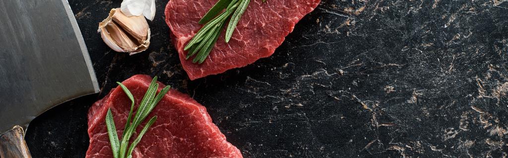 plan panoramique de steaks de boeuf non transformés avec brins de romarin près de l'ail et couteau sur la surface de marbre noir
 - Photo, image