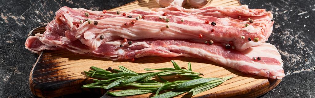 panoramic shot of wooden cutting board with raw pork slices sprinkled with peppercorns on black marble surface - Photo, Image