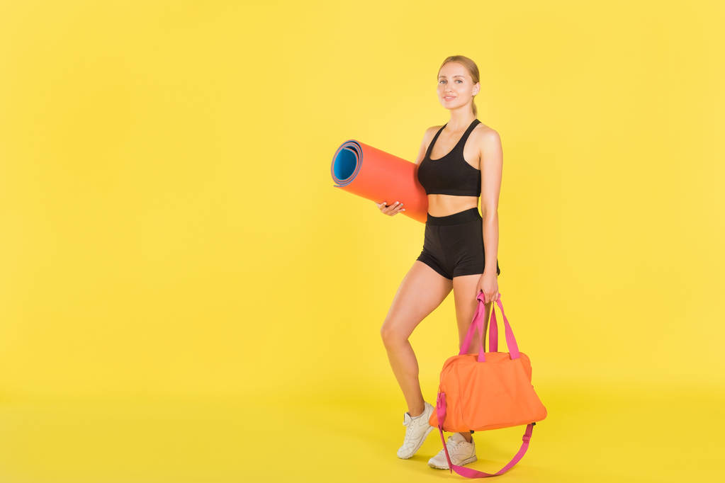 Femme avec un sac de sport et tapis de yoga sur fond jaune. Athlète femme
. - Photo, image