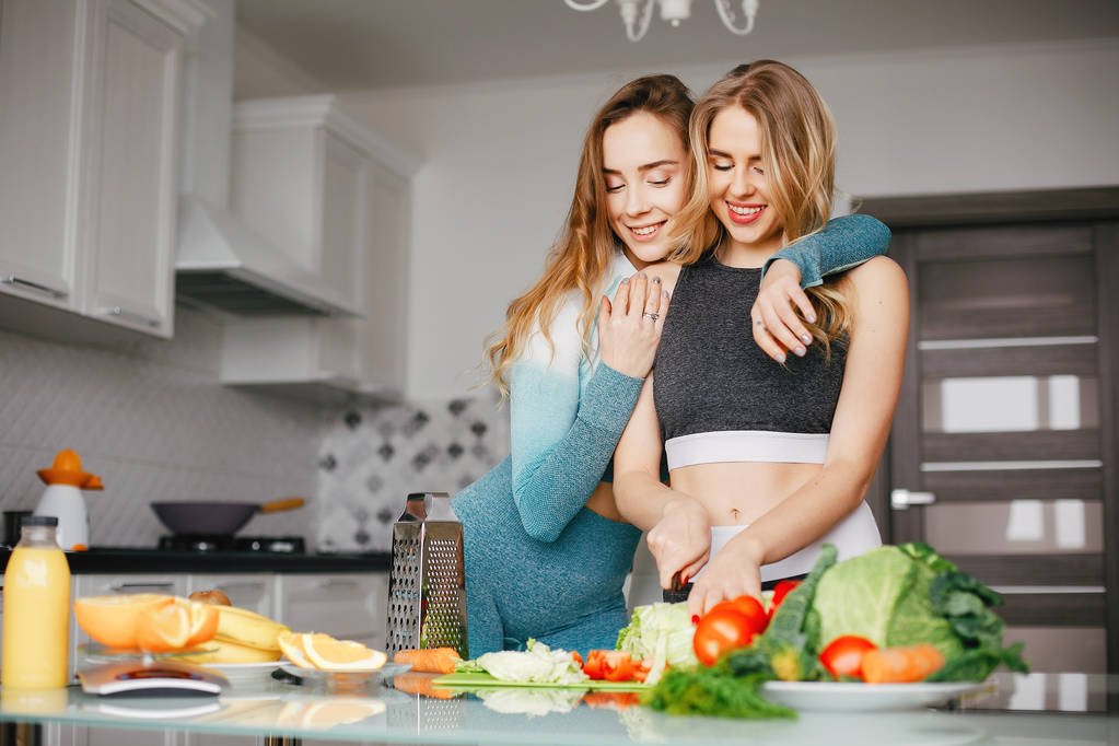 Twee sporten meisje in een keuken met groenten - Foto, afbeelding