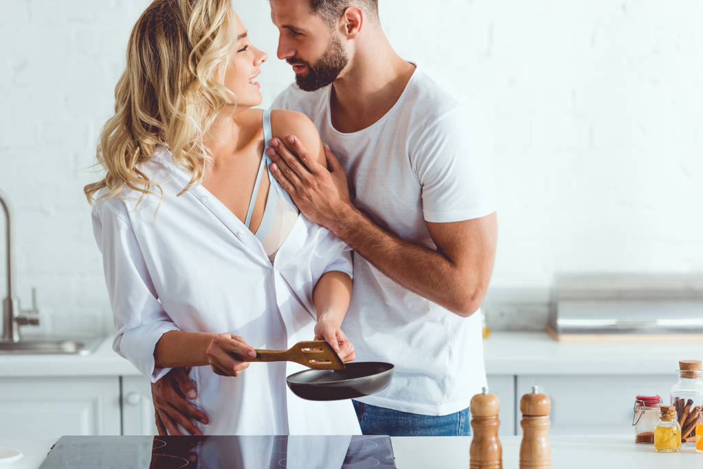 bello giovane uomo abbracciare allegra fidanzata preparare la colazione su padella
  - Foto, immagini