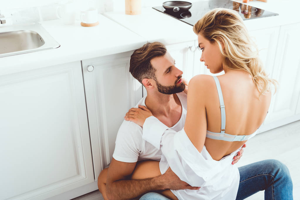 young couple hugging and looking at each other while sitting on kitchen floor - Photo, Image