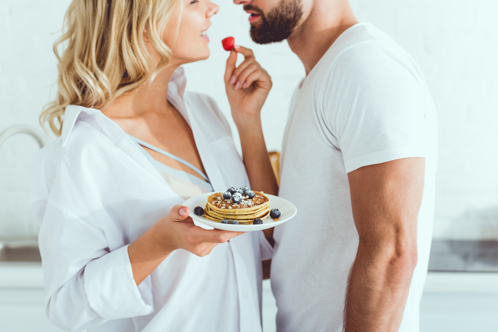 vista recortada de mujer joven sosteniendo plato con tortitas y fresa cerca de novio
  - Foto, imagen