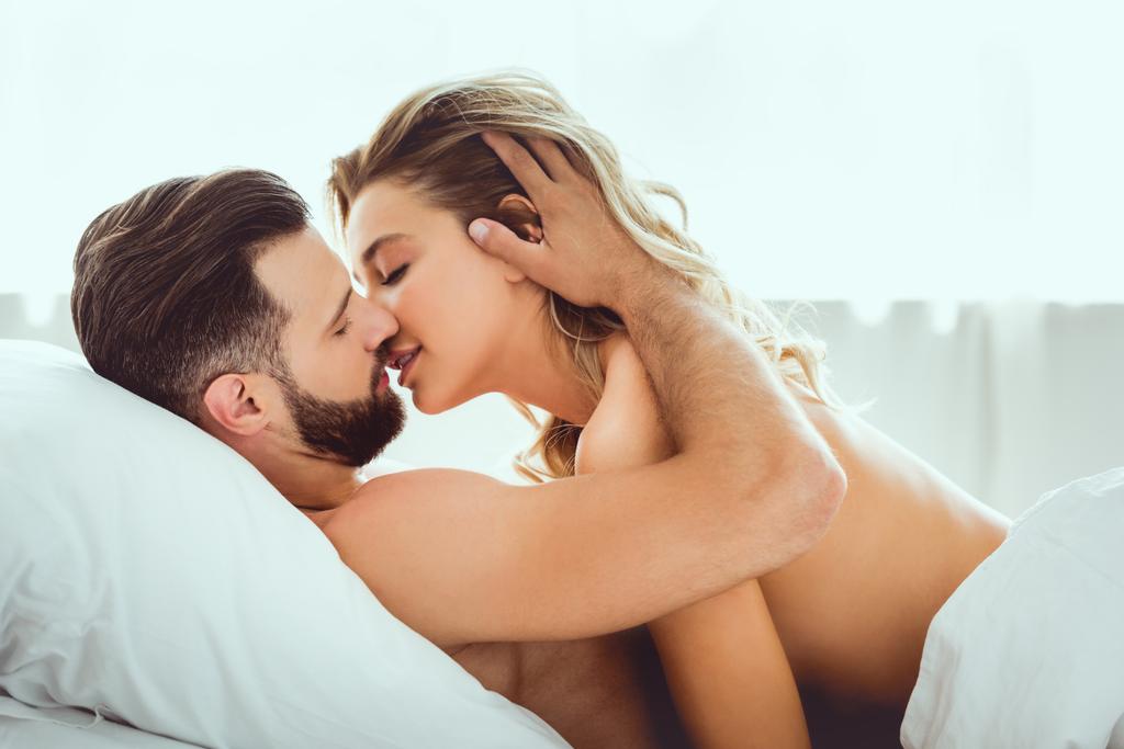 Красивый молодой человек целует красивую девушку, когда лежит в постели
 - Фото, изображение