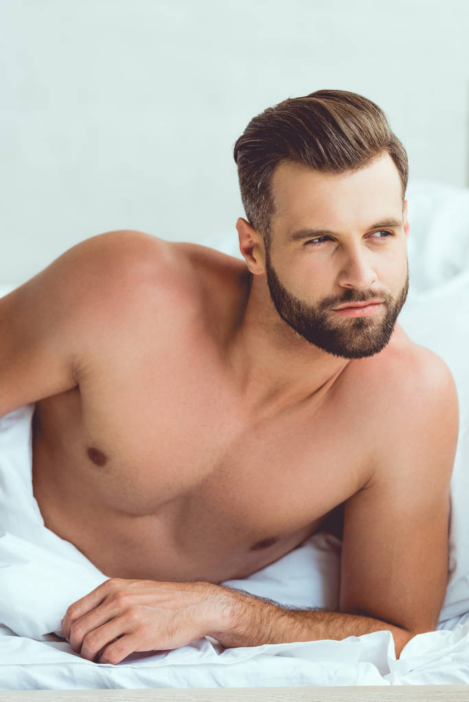 pensive, sexy man op zoek weg terwijl liggend in bed thuis - Foto, afbeelding